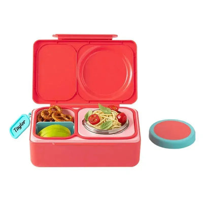 Bento box in cherry pink with compartments containing pasta, cherry tomatoes, pretzels, and an apple slice.