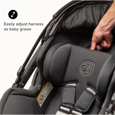 Rotating infant car seat with adjustable harness in Mélange Flax, showing hand adjusting the harness for growth.