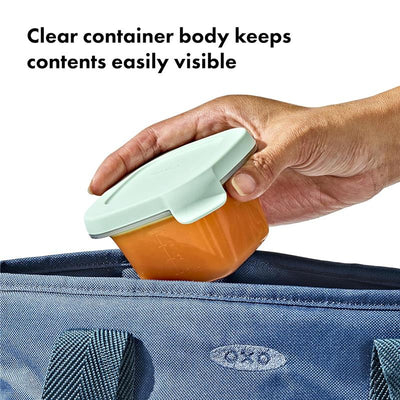 Clear silicone food storage container with a lid, showcasing orange contents, being placed in a blue bag.