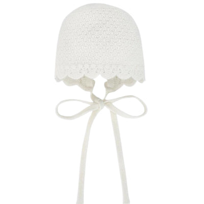 Knit newborn bonnet in chalk pink with scalloped edges and ribbon ties. Designed for babies.