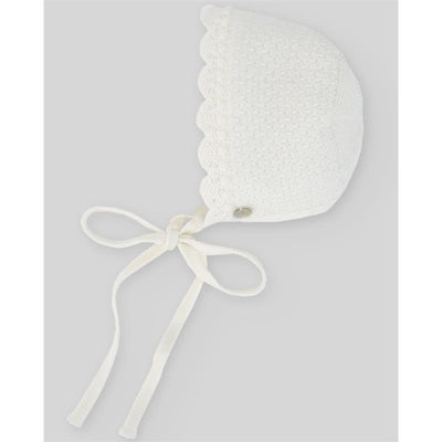 Baby knit bonnet in chalk pink with scalloped edges, ties under the chin, and a button detail on the side.