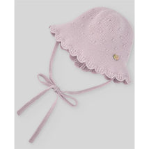 Knit newborn hat in mauve with scalloped edge and ties, featuring small textured dots and a decorative emblem.