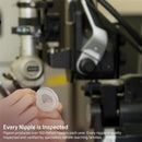 A person holds a clear baby bottle nipple, with quality inspection equipment visible in the background.
