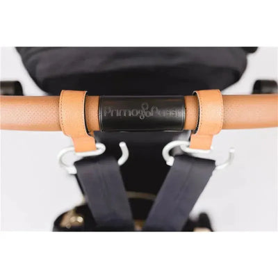Leather stroller hook in camel color, featuring a black Primo Passi logo and attached to a stroller handle for convenient use.