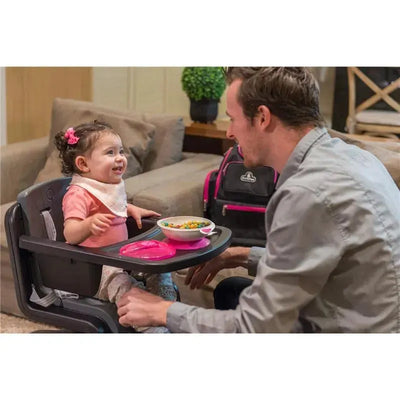 Toddler in a high chair wearing a bib, smiling at an adult, with a bowl of colorful cereal on a tray.