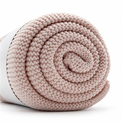 Light pink Primo Passi knit blanket rolled neatly, showcasing its soft texture and cozy design.