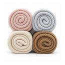 Light pink knit blanket among three other rolled blankets in gray, cream, and brown colors, showcasing soft texture and design.
