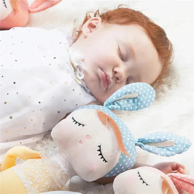 Sleeping baby girl with red curls, resting beside a blue polka dot plush doll with bunny ears.