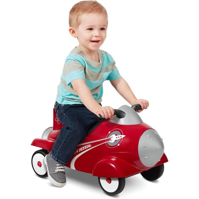 Toddler riding a red Radio Flyer Retro Rocket Ride-On Toy, smiling while holding the handlebars.