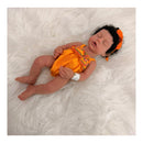 Reborn baby doll Arianna, an African American silicone doll, wears an orange outfit and a matching headband, resting on white fur.