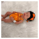 Reborn baby doll, Arianna, with African American features wearing an orange dress and matching headband, lying on a fluffy surface.