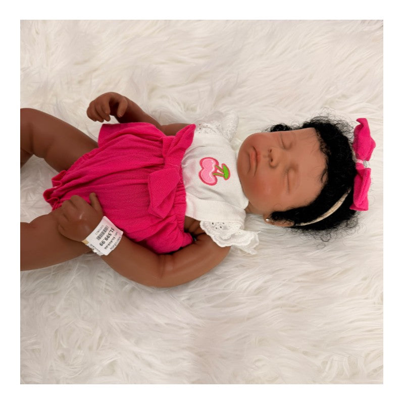 Reborn baby doll named Emily, featuring closed eyes, dark curly hair, wearing a pink outfit with a cherry design.