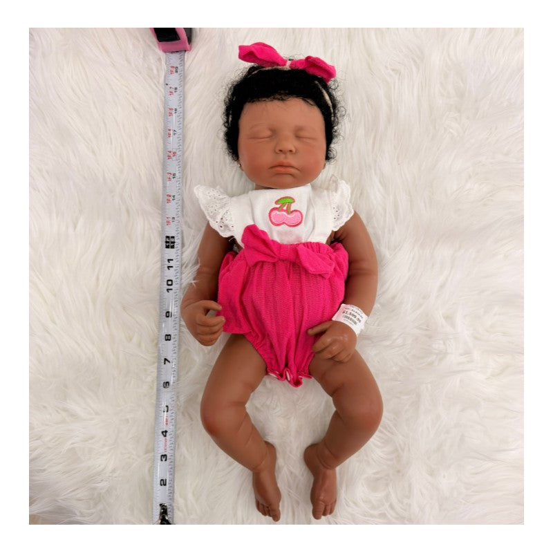 Reborn baby doll Emily, an African American full silicone doll with closed eyes, dressed in a white and pink outfit.