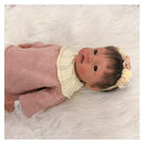 Reborn baby doll in a pink outfit with a cream collar and a flower headband, showcasing realistic features.