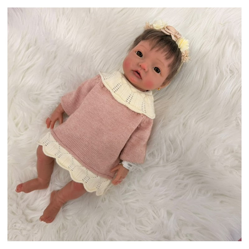 Reborn baby doll dressed in a pink sweater dress with a lace hem, featuring a headband with flowers.