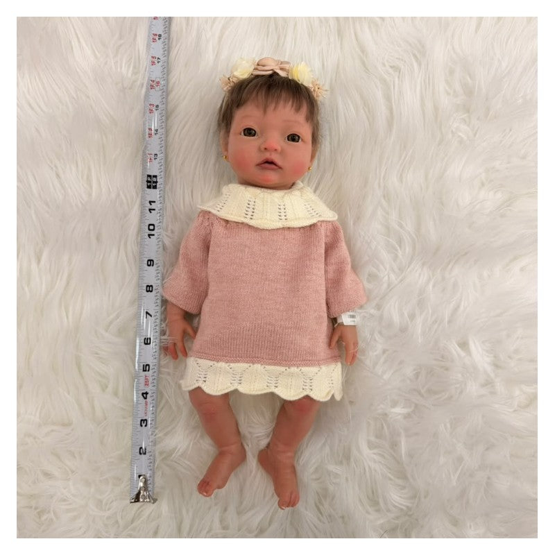 African American silicone reborn baby doll wearing a pink sweater dress with a white collar, measuring tape alongside.