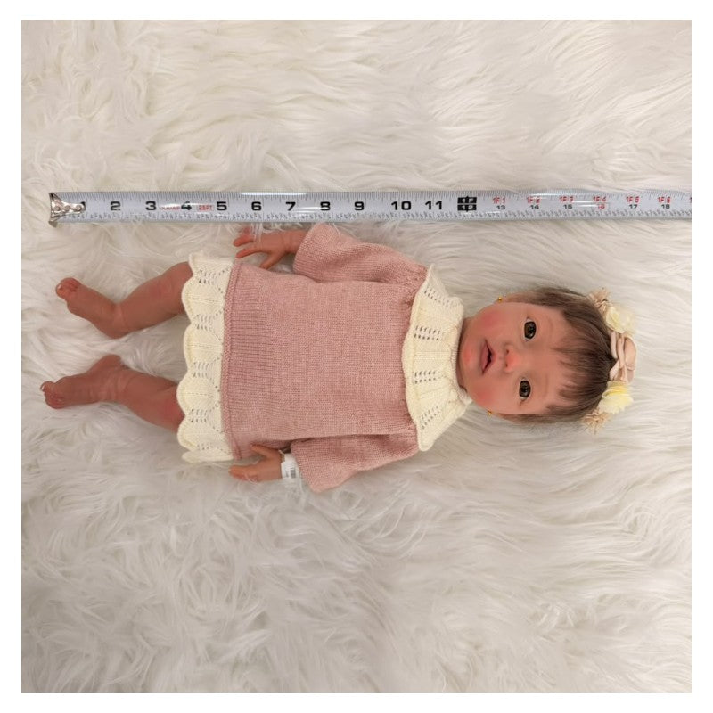 Reborn baby doll with African American features, wearing a pink dress and headband, placed on a fluffy white surface.