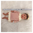 Reborn baby doll with African American features, wearing a pink dress and headband, placed on a fluffy white surface.
