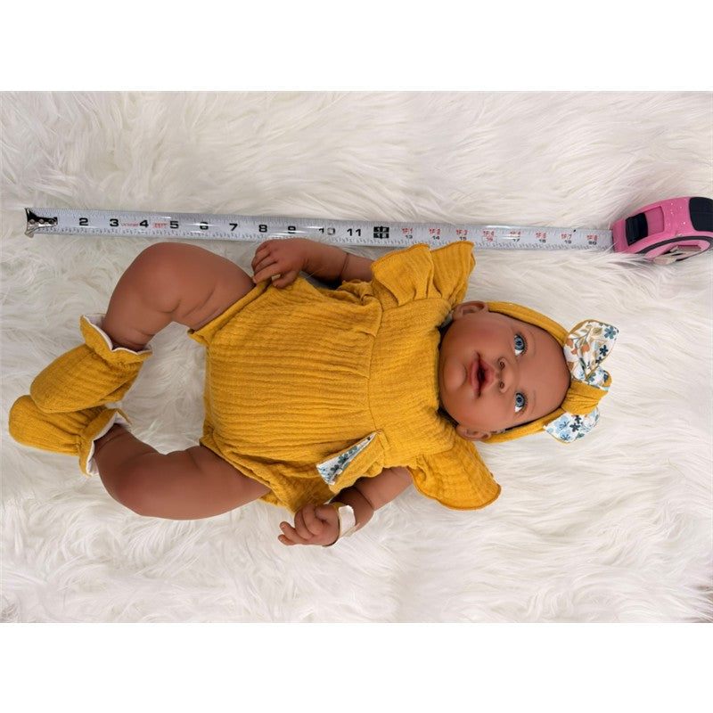 Reborn baby doll with dark skin wears a yellow outfit and matching headband, measuring tape visible beside it.