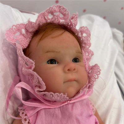 Reborn Baby Doll Bettie, featuring a full silicone body, wears a pink bonnet and dress, with delicate facial details.