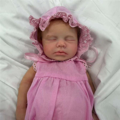 Reborn baby doll named Charlie, featuring a full silicone body, wearing a pink dress and bonnet, with closed eyes and a peaceful expression.