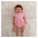 Reborn baby doll Vivienne, featuring a full silicone body, dressed in a pink outfit with lace detailing and a matching headband.