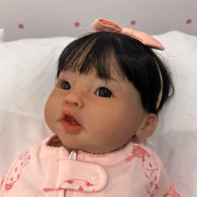 Reborn baby doll with realistic features, wearing a pink outfit and a hair bow, showcasing lifelike expression and details.