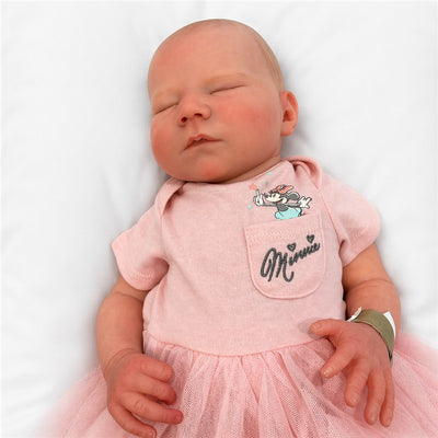 A lifelike reborn baby doll with white vinyl skin, dressed in a pink outfit featuring Minnie Mouse and a tulle skirt.