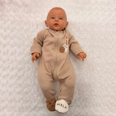 Reborn baby doll in a striped onesie with a milk and cookie motif, wearing milk-themed booties, against a soft background.