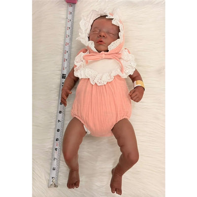 Reborn Baby Doll named Bryan, featuring African American vinyl skin and dressed in a pink and white outfit with a lace trim.