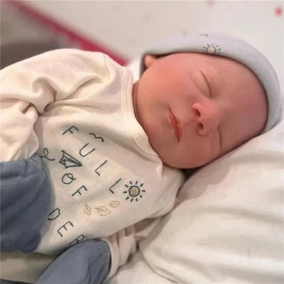 Reborn Baby Doll named June, featuring vinyl skin, wearing a light blue hat and a cream shirt with the text “FULL OF WONDER.”