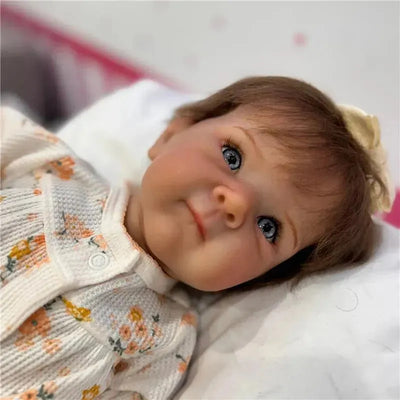 Reborn baby doll named Bettie with white vinyl skin, blue eyes, and a floral-patterned outfit.