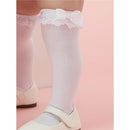 Knee-high white socks featuring lace ruffles and bows, styled with a pair of white shoes on a pink background.