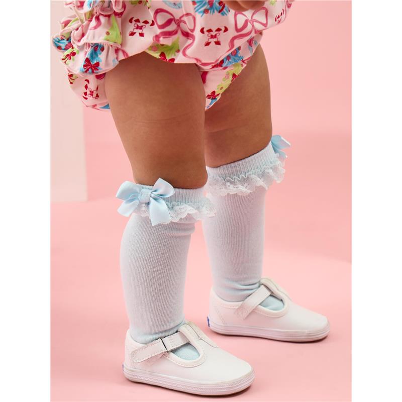 Knee-high socks in light blue with lace and bows, worn by a toddler alongside white shoes and a colorful floral outfit.