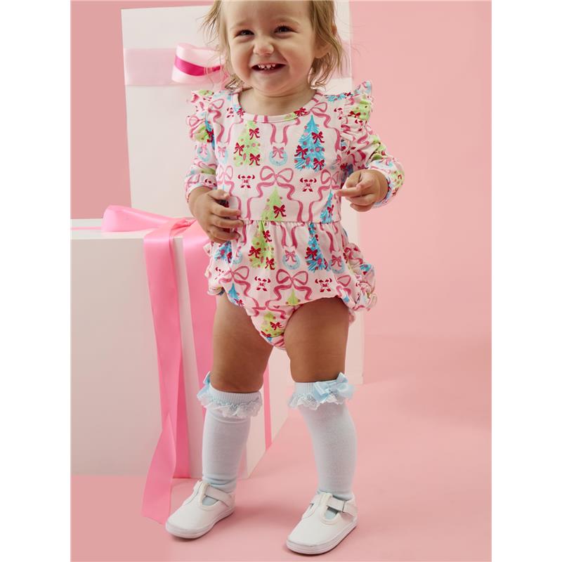 Toddler smiling while wearing a colorful romper and lace ruffle knee-high socks, standing near gift boxes.