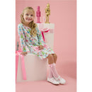 Knee-high pink socks with lace and bows worn by a girl in a colorful, festive dress, sitting on a pedestal with decorations.