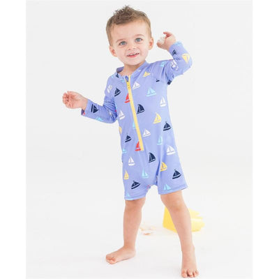 Baby boy wearing a light purple long sleeve rash guard swimsuit with colorful sailboat prints, smiling and playing.
