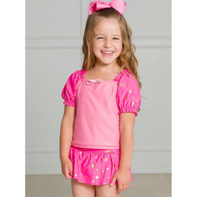 Baby girl smiling in a royal pink puff sleeve skirted swimsuit with gold star accents.
