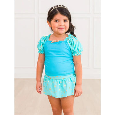 Baby girl wearing a teal puff sleeve swimsuit with a gold star print skirt, smiling, with a tiara in her hair.