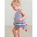 Baby girl wearing a blue and white striped swing top with red and blue ric rac trim, paired with matching ruffle bloomers.