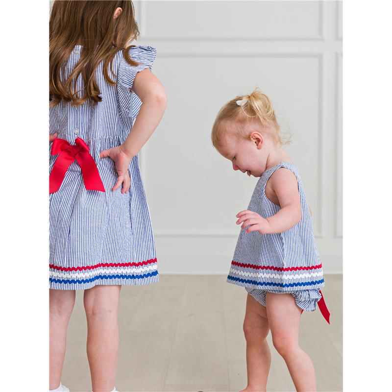 Two young girls wearing Americana-themed outfits: one in a blue seersucker dress with a red bow, and the other in a matching ruffle bloomer set, both with striped patterns.