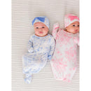 Two infants in butterfly-patterned sleep gowns and matching bow hats, one blue and one pink, lying on a textured white surface.