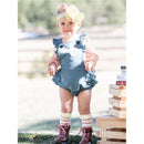Toddler girl wearing a blue ruffle romper and ivory big bow headband, posed outdoors with playful boots and colorful socks.