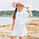 White terry cover-up for infants with pink seersucker accents, worn by a smiling girl by the water in a sun hat.