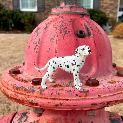 Dalmatian figurine standing on a weathered red fire hydrant in a grassy area.