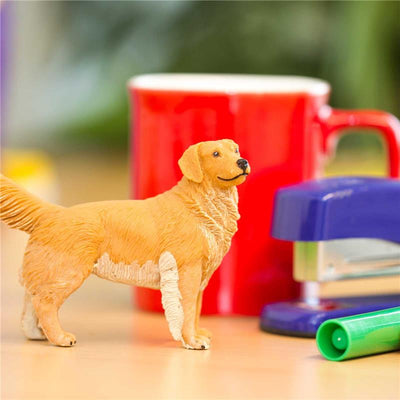 Golden Retriever plastic model figure in front of a red mug, stapler, and green marker on a desk.