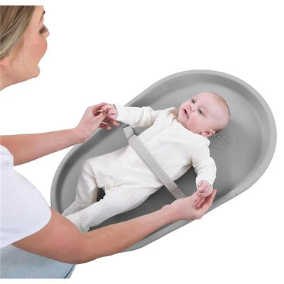 Squishy grey baby changing pad with a secured infant wearing a light onesie, being gently held by an adult.