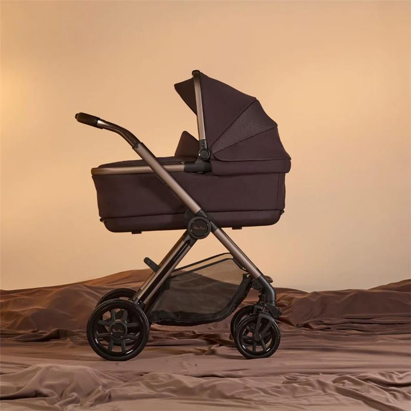 Silver Cross Reef 2 Folding Bassinet in Ganache color with a sleek frame and adjustable canopy, set on a textured surface.