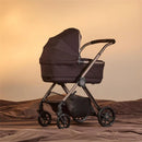 Silver Cross Reef 2 Folding Bassinet in Ganache color, featuring a sturdy frame and four wheels, set against a soft beige background.