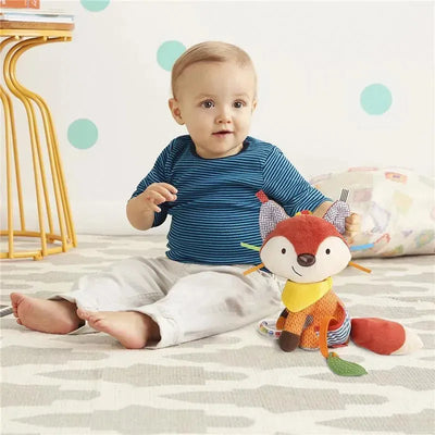 A baby wearing a blue striped shirt sits on a patterned rug next to the Skip Hop Bandana Buddies Fox stroller toy, featuring colorful textures and features.